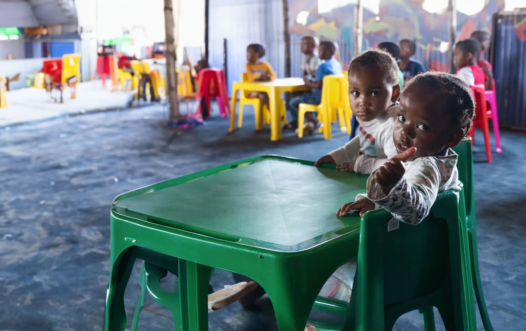 Two young children at a pre-school table, looking towards the camera