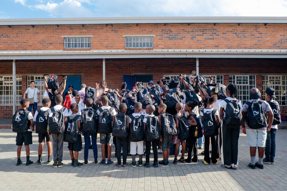 Learners outside their school holding up new Liberty Compassion backpacks
